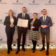 Zdjęcie przedstawiające Zarząd Blisko Krakowa na tle ścianki Województwa Małopolskiego. Od lewej Wiceprezes Agata Kowalska, Prezes Michał Kędzierski, Skarbnik Małgorzata Tomczyk, Wiceprezes Stanisław Kozioł